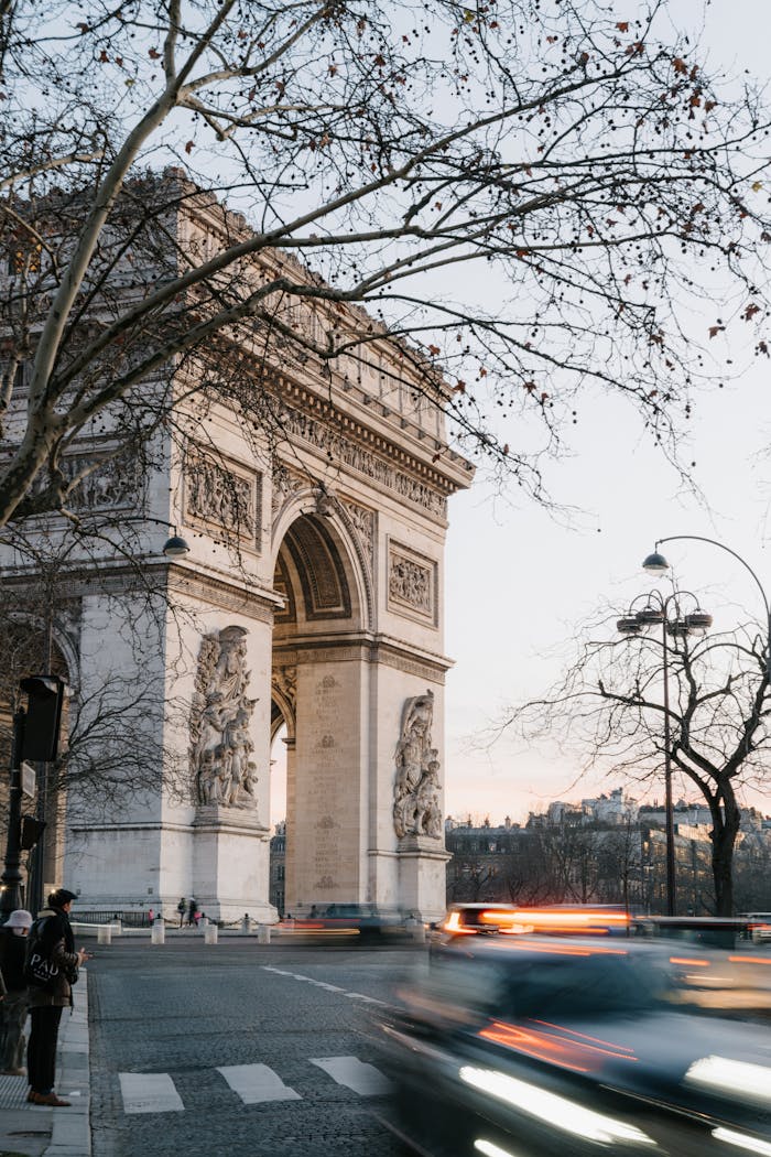 View of the Arc de Triomphe in Paris at dusk with blurred car motion and winter trees.